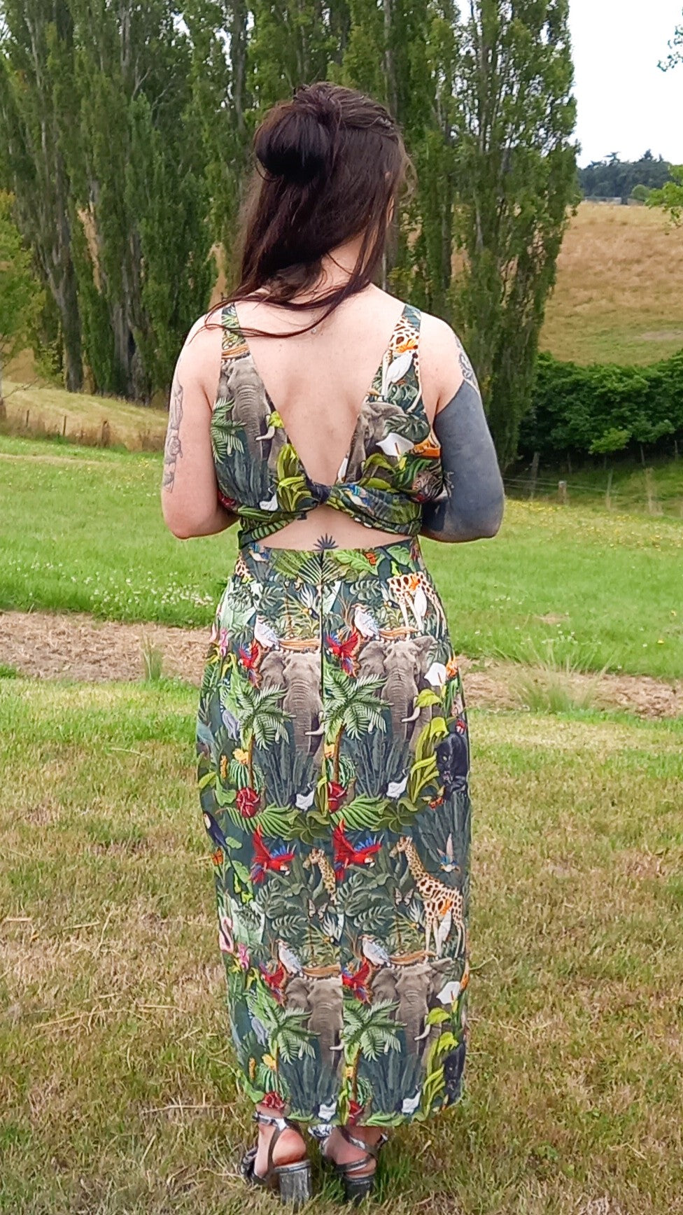 Back of tattooed woman wearing safari print rental dress set with waist tie and pencil skirt in countryside