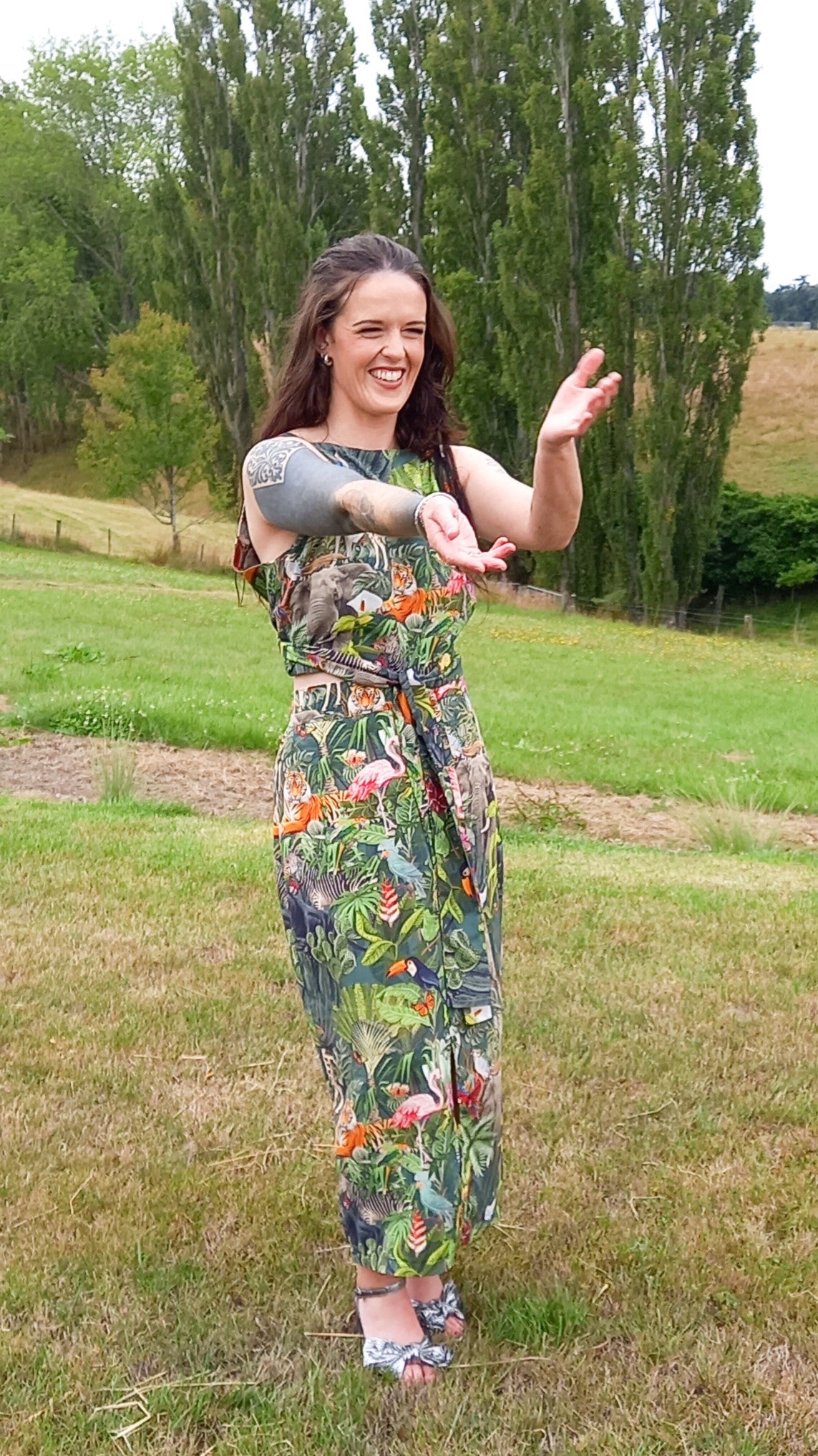 Tattooed woman dancing wearing safari print rental dress set with waist tie and pencil skirt in countryside